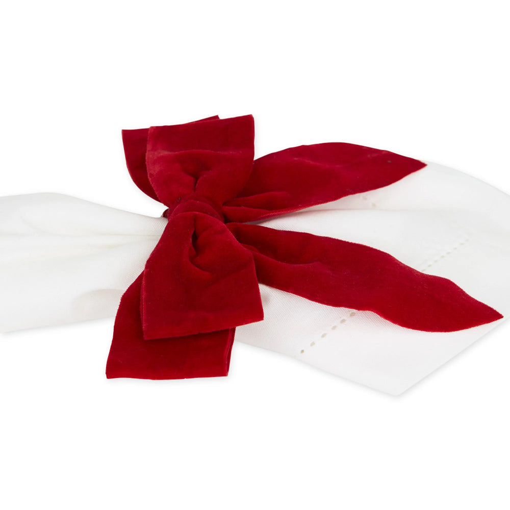 A deep red velvet bow tied neatly on a white fabric napkin, set against a seamless white background.