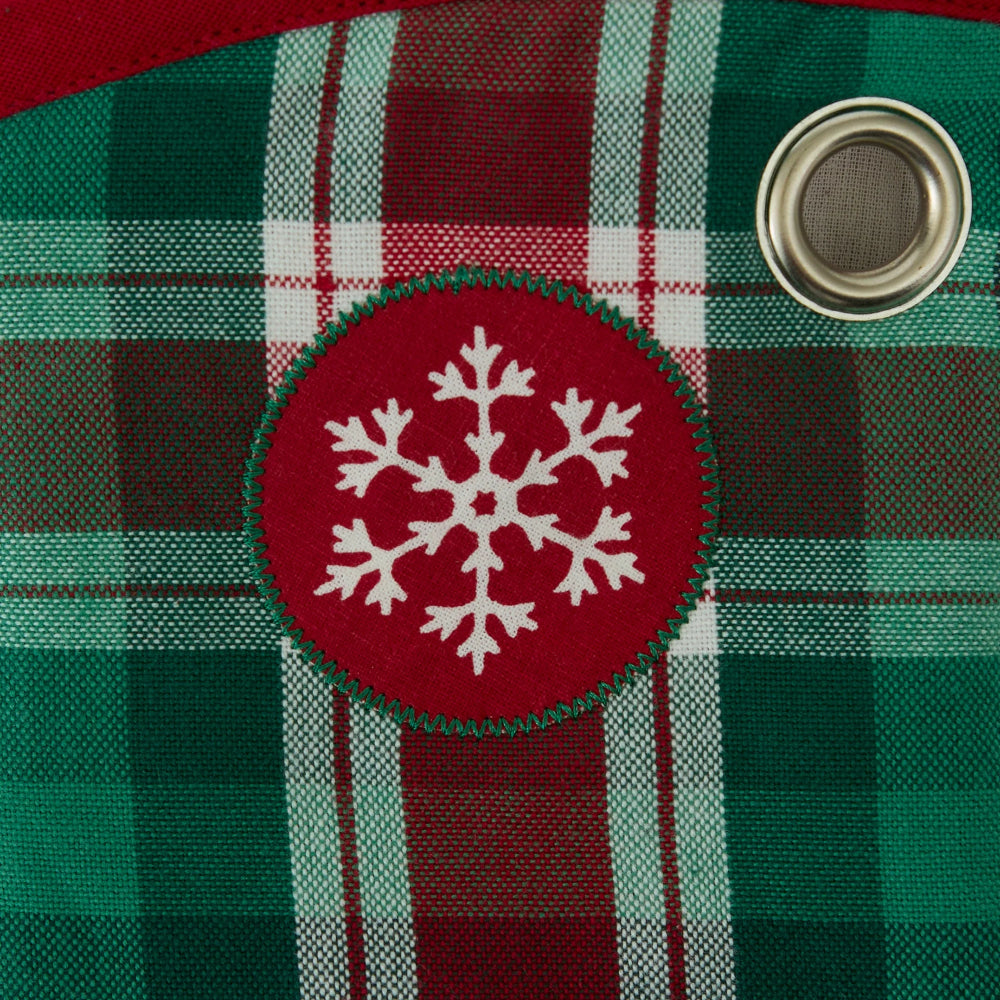 Close-up of a red and green plaid fabric with a circular red patch featuring a white snowflake design and a metal grommet.