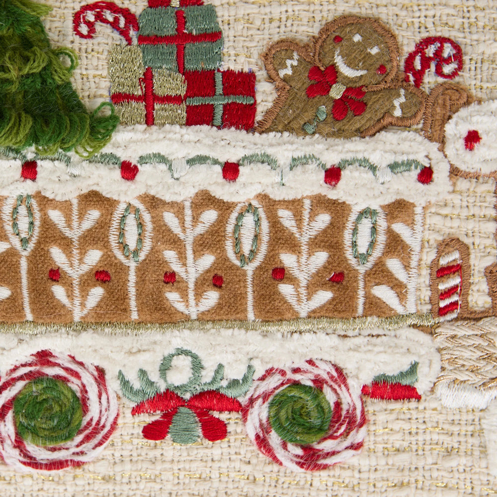 Close-up of a handcrafted embroidered textile featuring gingerbread-themed motifs, including a gingerbread man, wrapped gifts, candy canes, and floral patterns in brown, red, green, and cream on a woven fabric background.