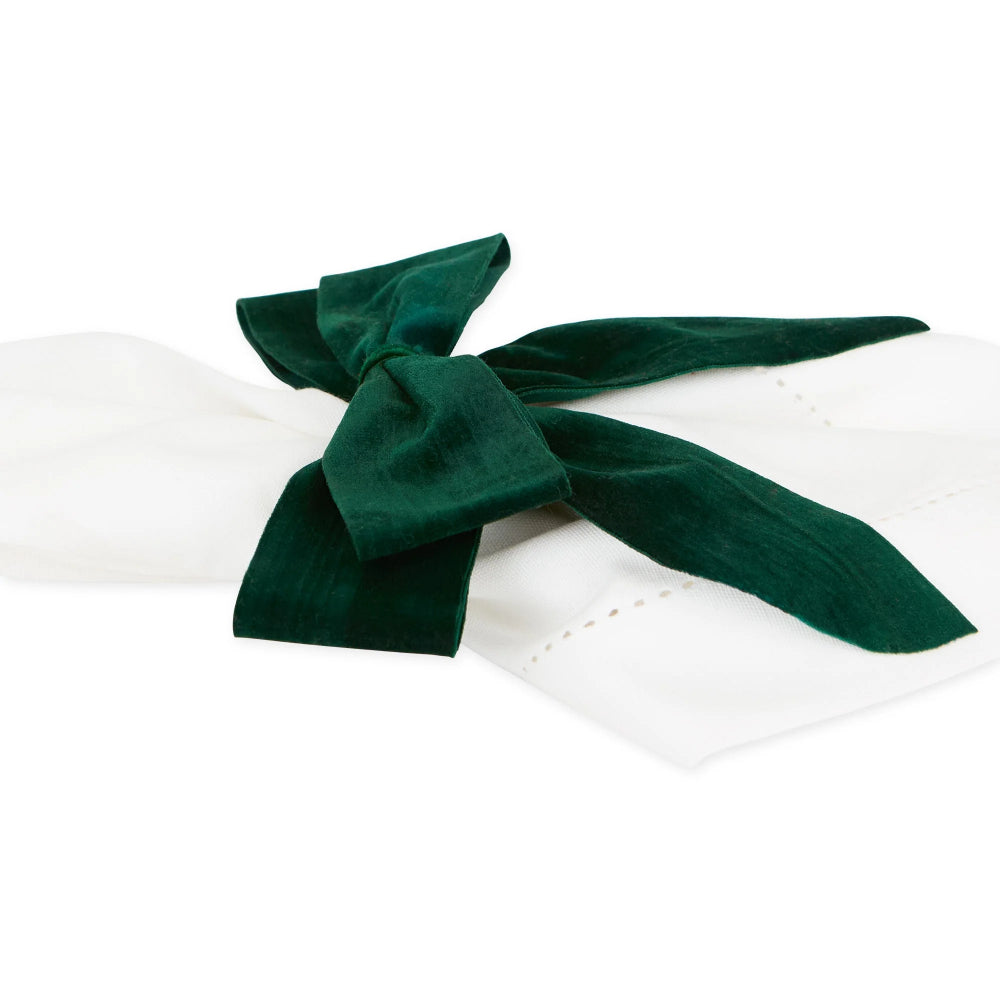 A dark green velvet napkin ring tied around a white paper napkin, shown on a clean white background.