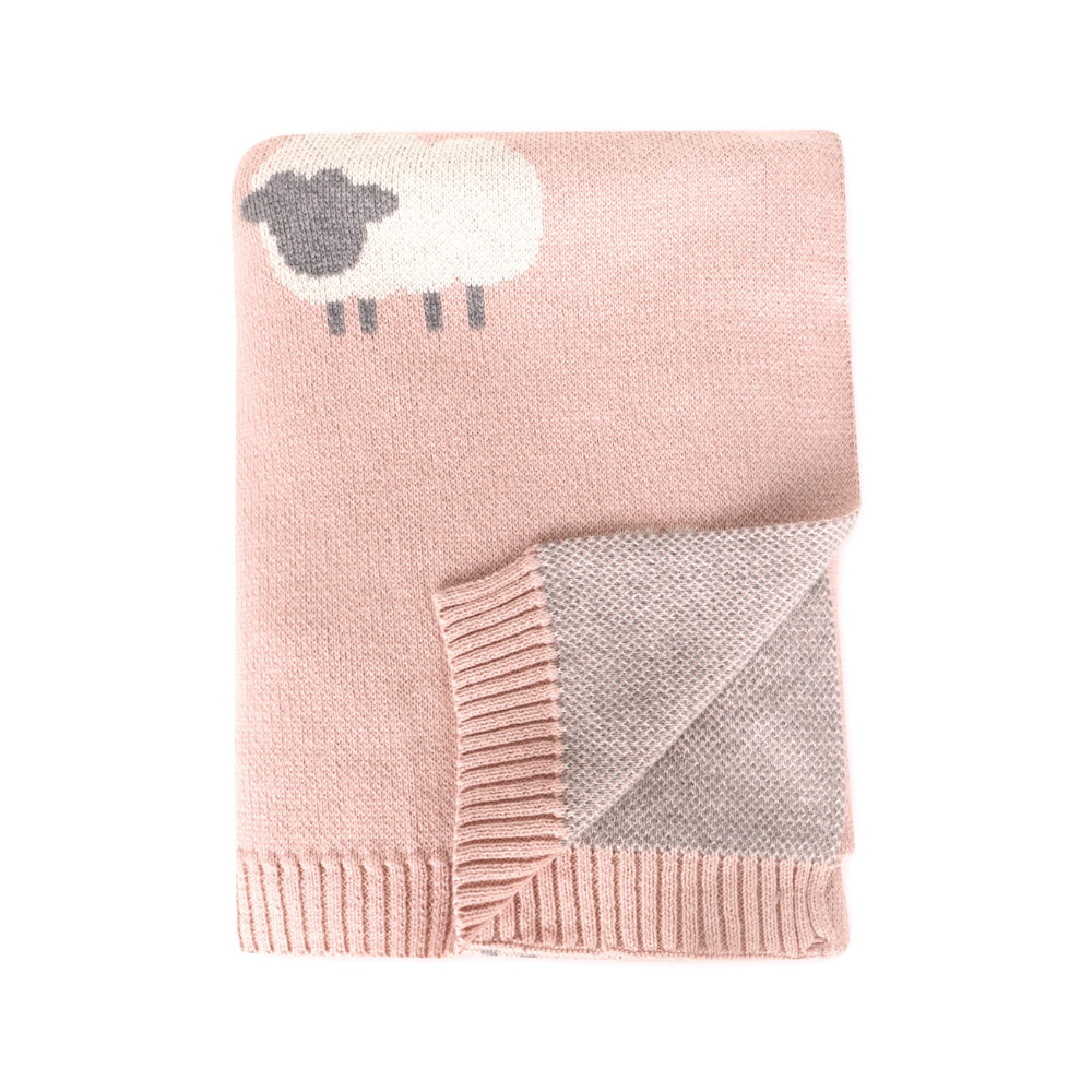 A folded pink knit blanket featuring a white sheep motif with a dark gray head on the upper left, and a folded corner revealing a lighter gray reverse side with ribbed trim.
