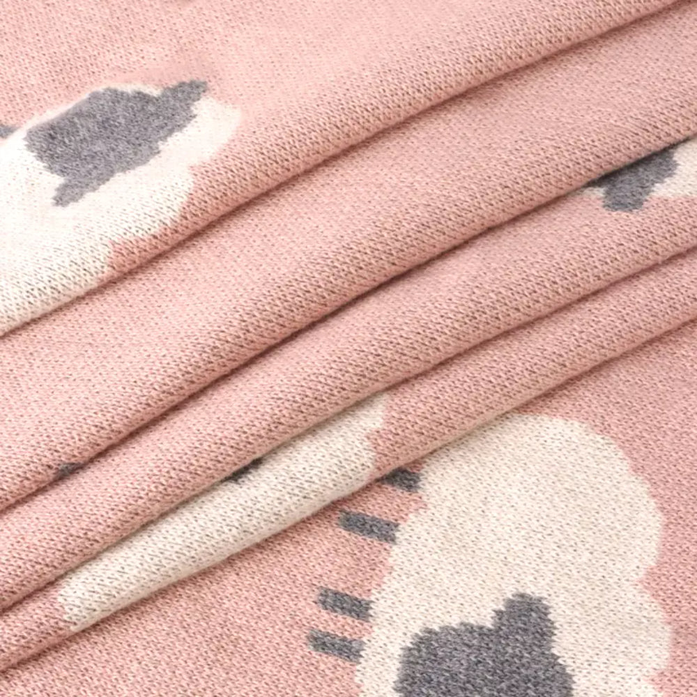 Close-up of pink blanket with white lamb designs on it. 