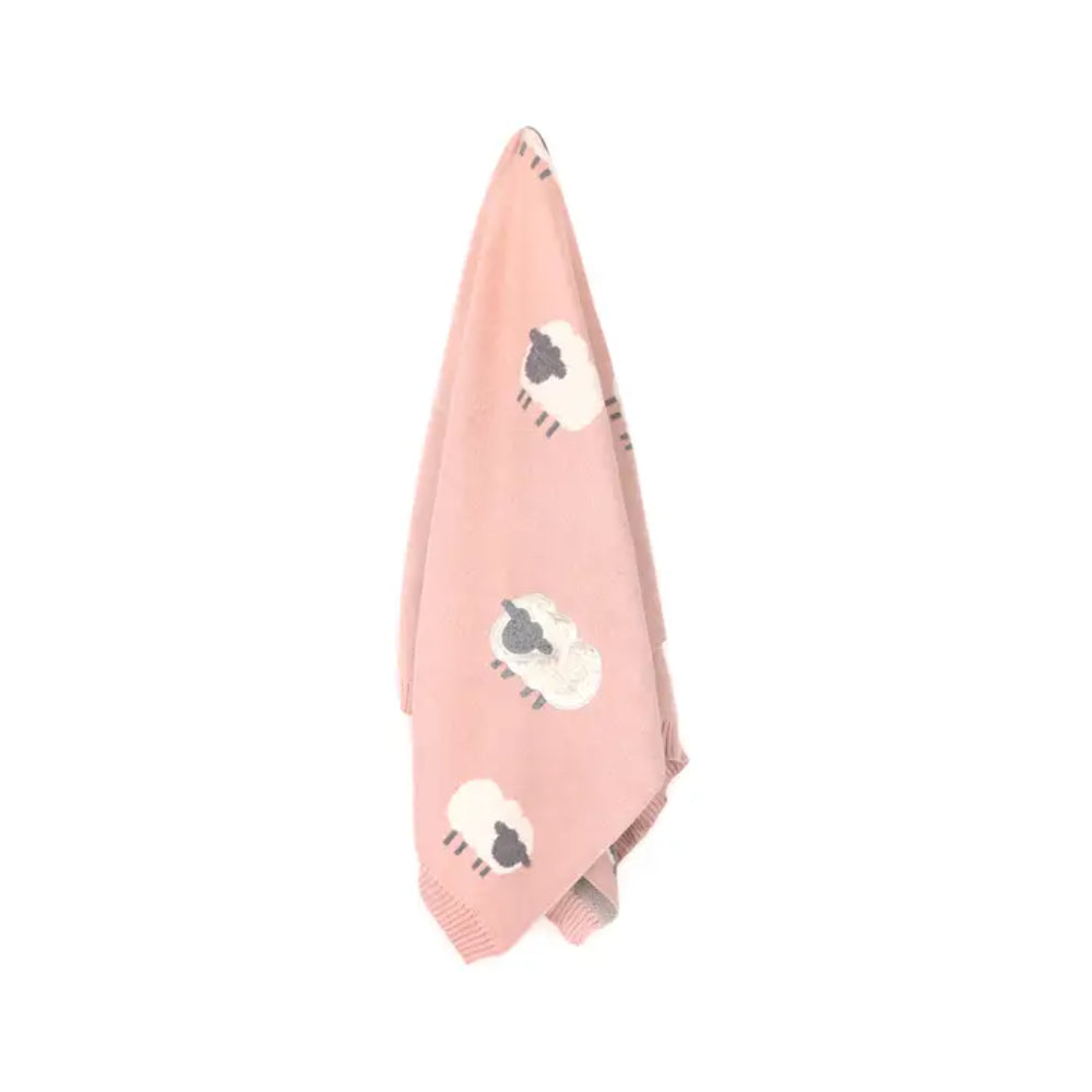 Pink towel with white lamb designs hanging on a white background.