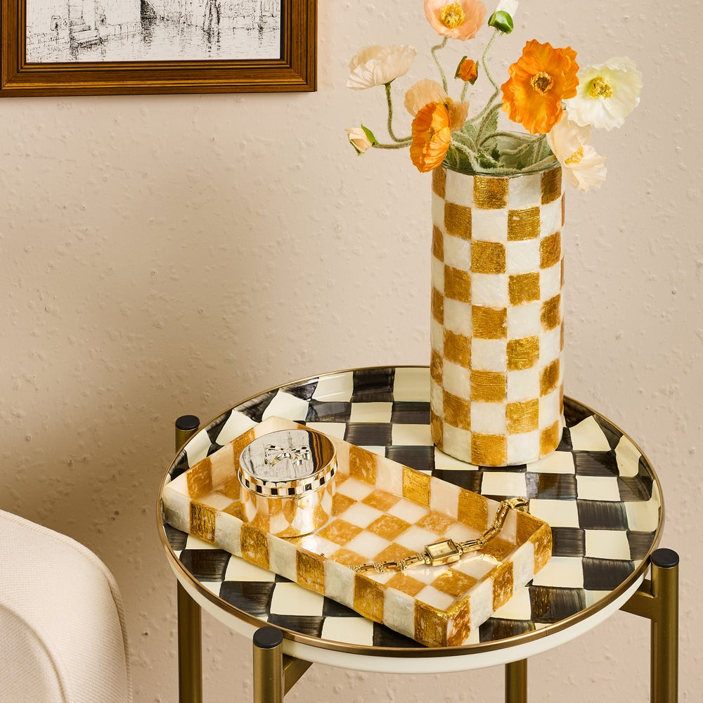 Black and white checkered round side table with gold and white checkered vase and tray with silver round keepsake box on tray. 