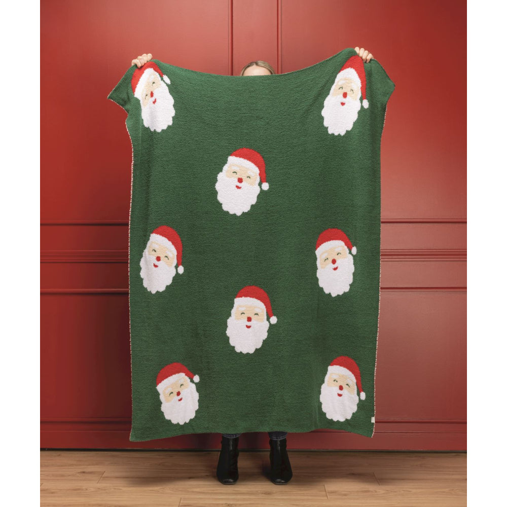Person holding a green blanket with Santa Claus patterns against a red wall.
