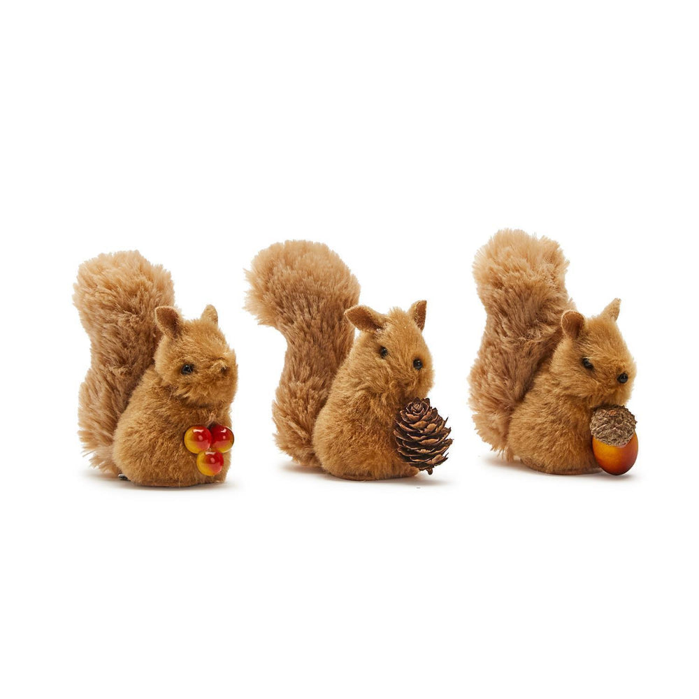 Three toy squirrels with pinecones and acorns on a white background