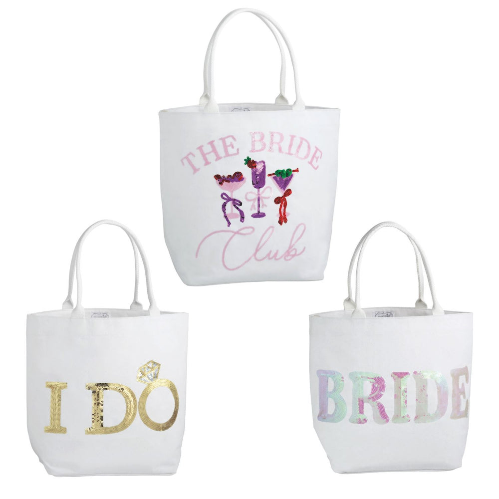 Three white canvas tote bags with bridal-themed designs on a plain white background. The top bag reads 'THE BRIDE Club' with cocktail illustrations, the bottom left reads 'I DO' in gold glitter, and the bottom right reads 'BRIDE' in pastel glitter.