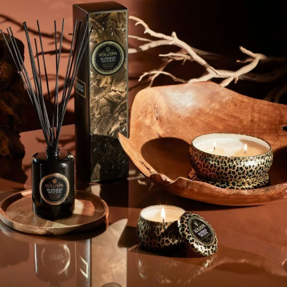 Black burning woods diffuser on a brown table with brown decor and two tin candles. 