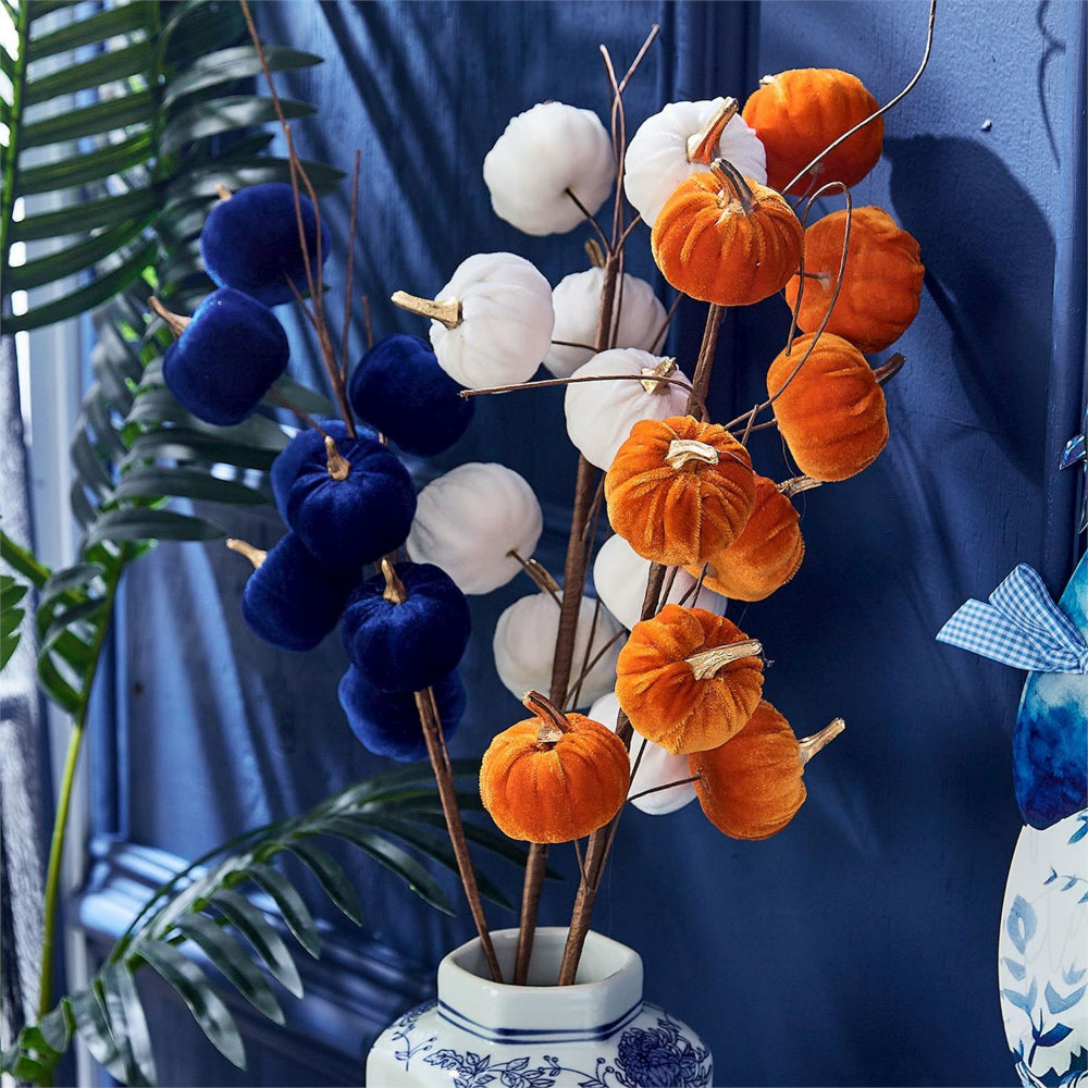 Decorative artificial pumpkins and cotton bolls in a white ceramic vase with blue floral patterns, set against a dark blue background with tropical leaves.