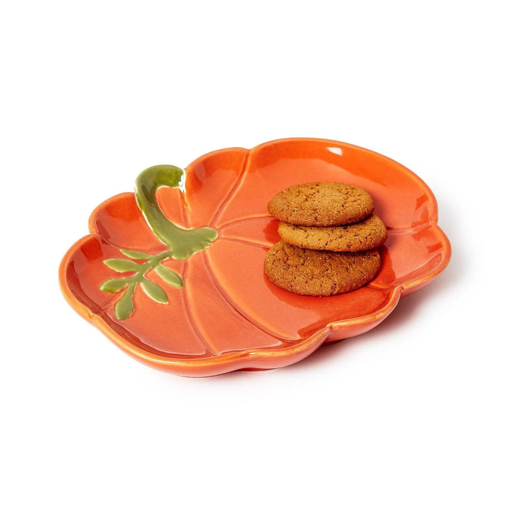 An orange ceramic cookie dish shaped like a pumpkin with a green stem holding three cookies, on a white background.