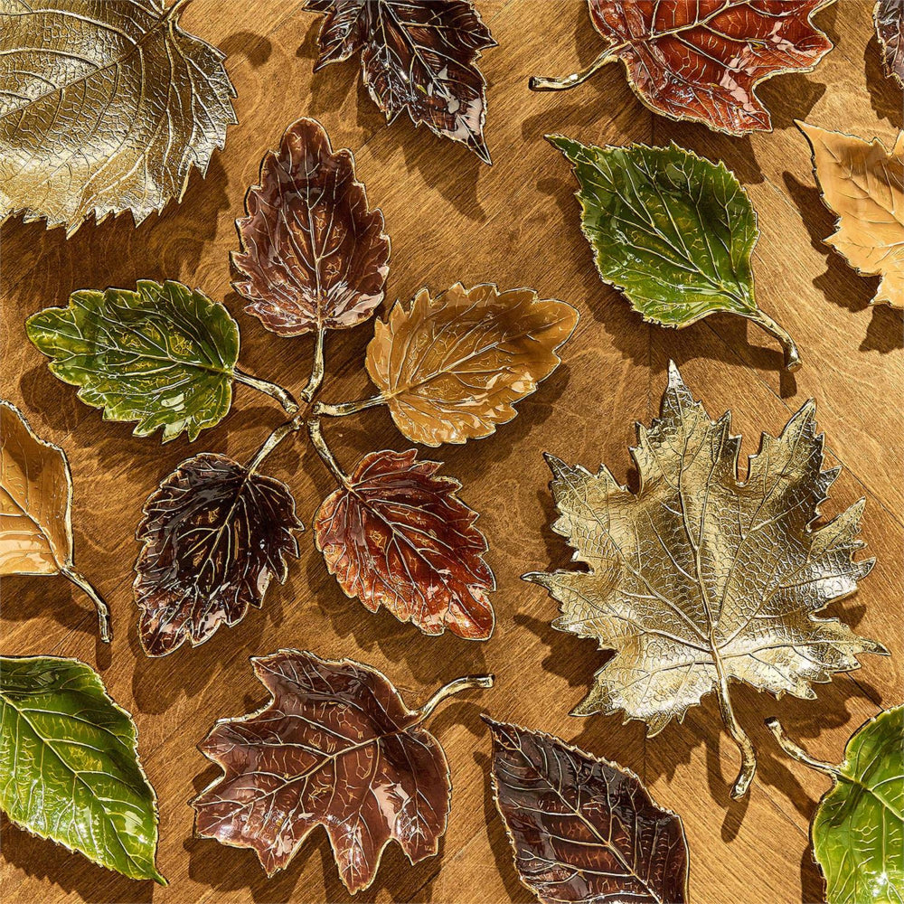 Decorative faux autumn leaves arranged on a wooden surface, featuring realistic textures and colors in green, brown, bronze, and gold.