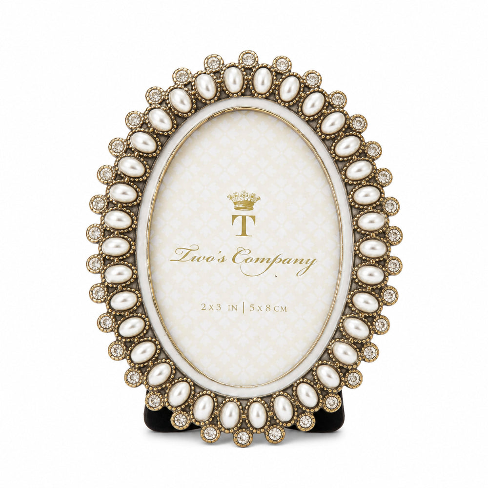 An oval picture frame with a decorative gold-tone border featuring faux pearls and clear rhinestones, displayed on a black stand against a white background. The center insert shows the brand logo 'Two's Company'.