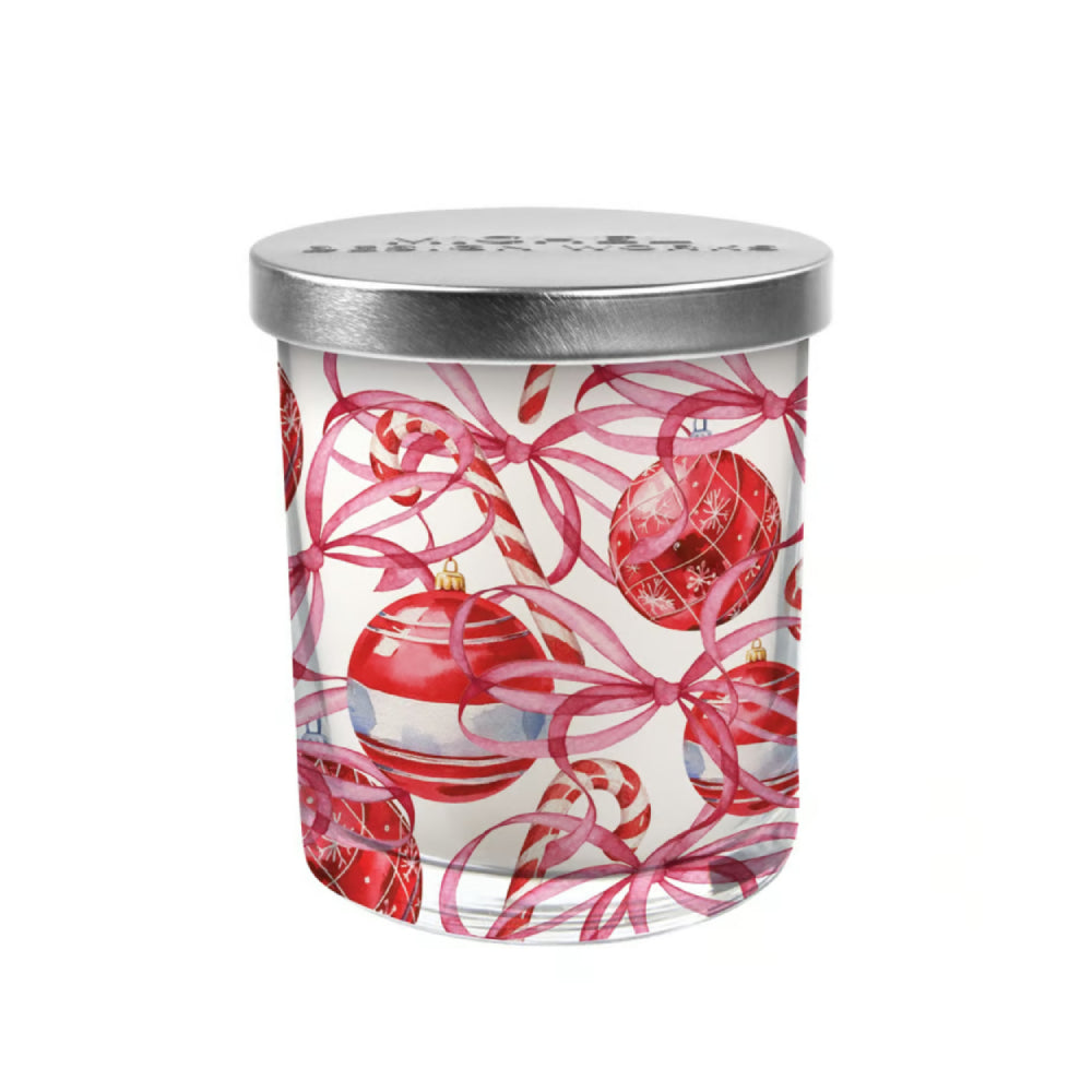 A glass jar candle with a silver metal lid, decorated with a festive Christmas pattern of red ornaments, pink ribbons, and candy canes on a white background.