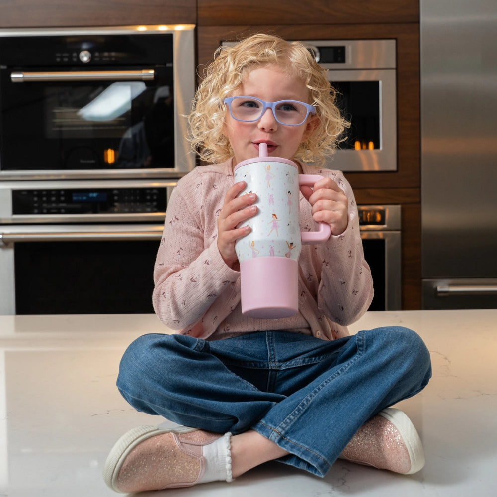 Child sitting on a kitchen counter drinking from a pink tumbler cup.