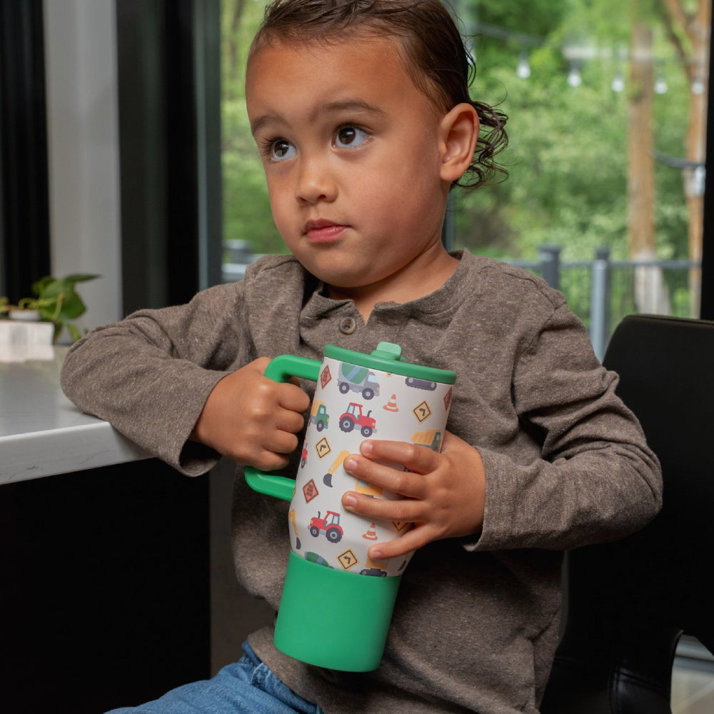 Child holding a colorful tumbler with a pattern of vehicles and nature.