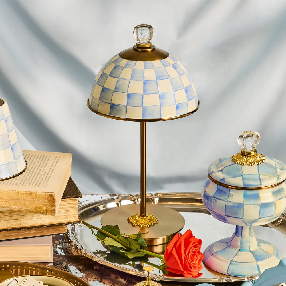 Decorative table lamp with checkered design on a reflective surface with books and a rose.