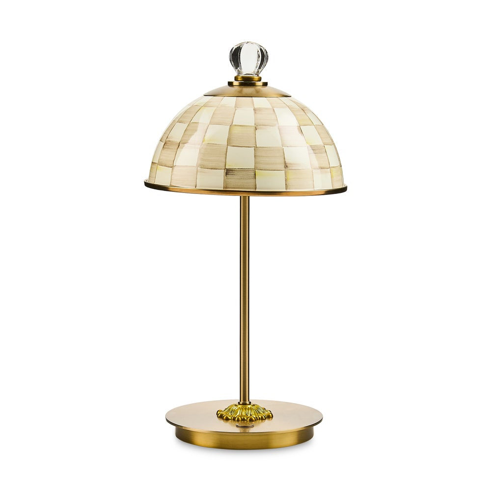 A table lamp with a dome-shaped shade made of cream and beige mocha check, supported by a polished gold brass stand with a round base and a clear glass finial on top.