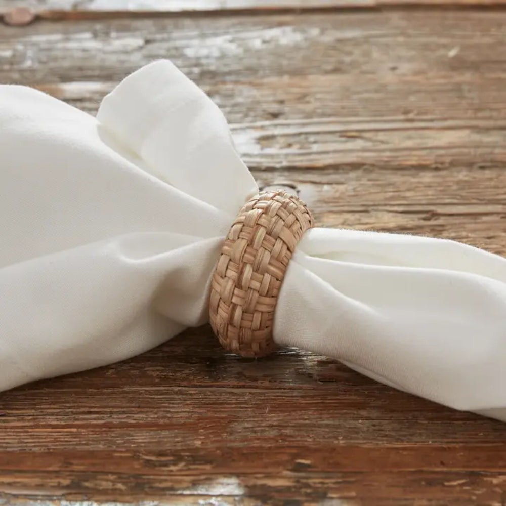 Rattan Woven Napkin Ring around white napkin on wooden surface display. 