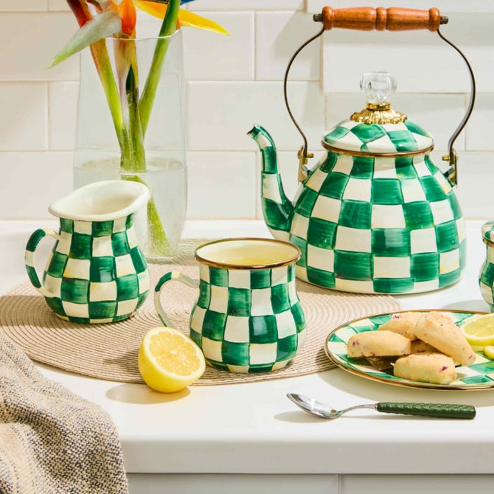Green and white checkered teapot, pitcher, and mug on a kitchen counter with lemon slices and cookies.