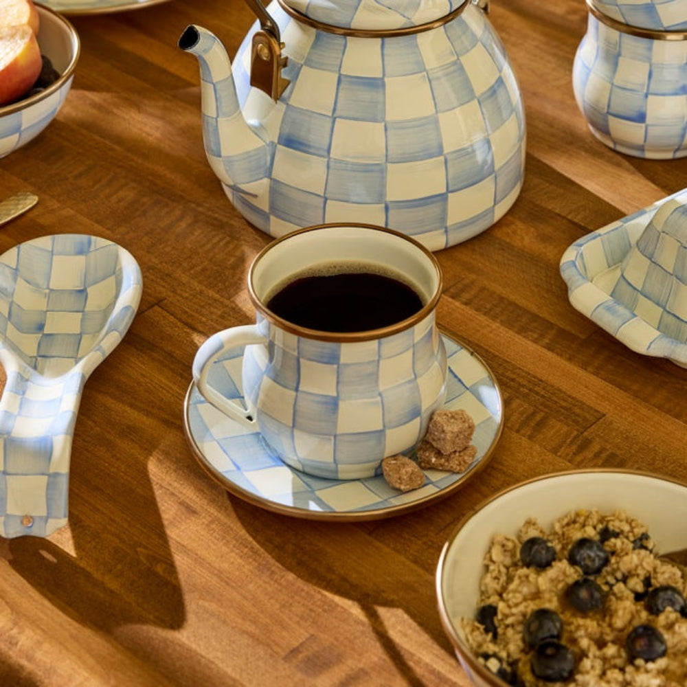 Sky Check Mug with coffee in it placed on top of Sky Check Plate nd surrounded by Sky Check Spoon Rests, Butter Dishes, Tea Kettles, and Bowls on a wooden surface. 