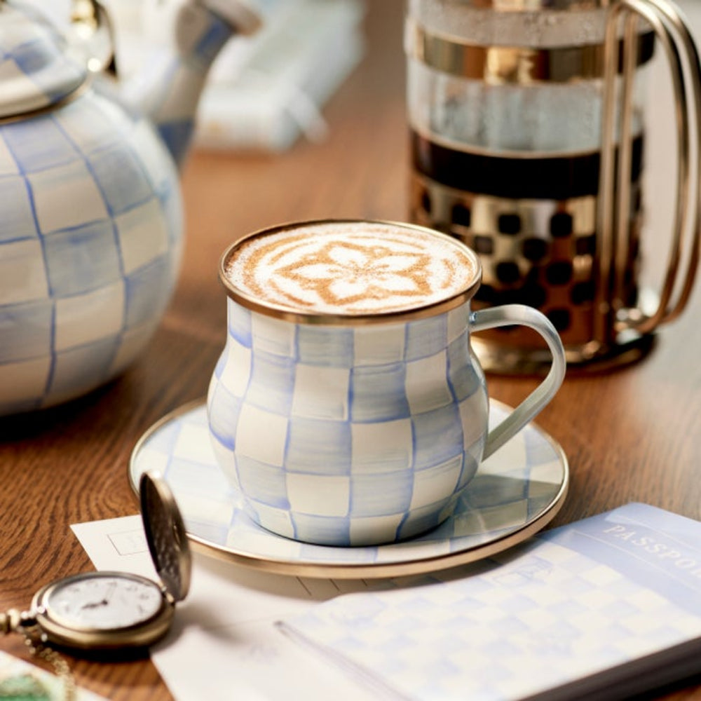 Sky Check Mug with coffee beverage in it with flower logo design. Mug surrounded by Sky Check tea kettle on a wooden surface. 