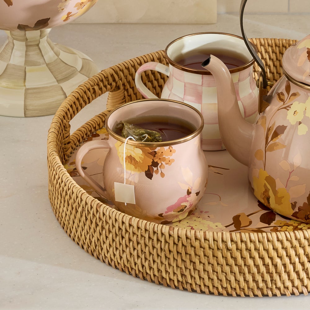 Floral-patterned teapot and mugs on a Pink Floral-patterned surface in a woven basket tray. 