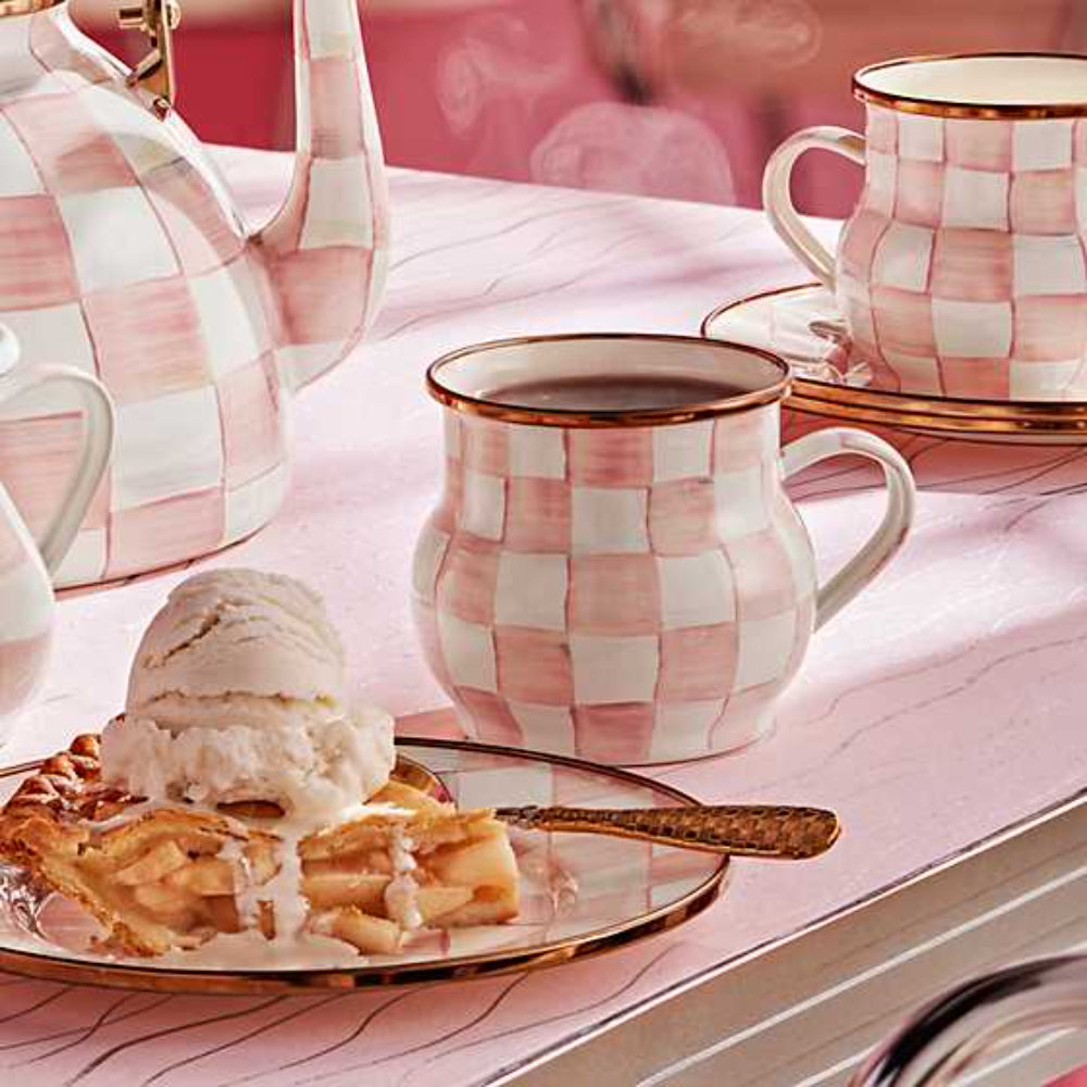 Mug with rosy pink and white checkered pattern and gold rim on a a table with a pink background. 