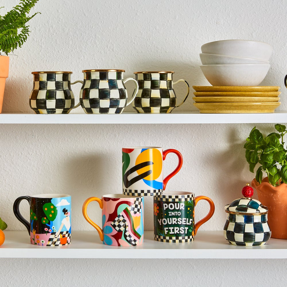 Colorful mugs and a checkered jar on a white shelf with a white wall background.