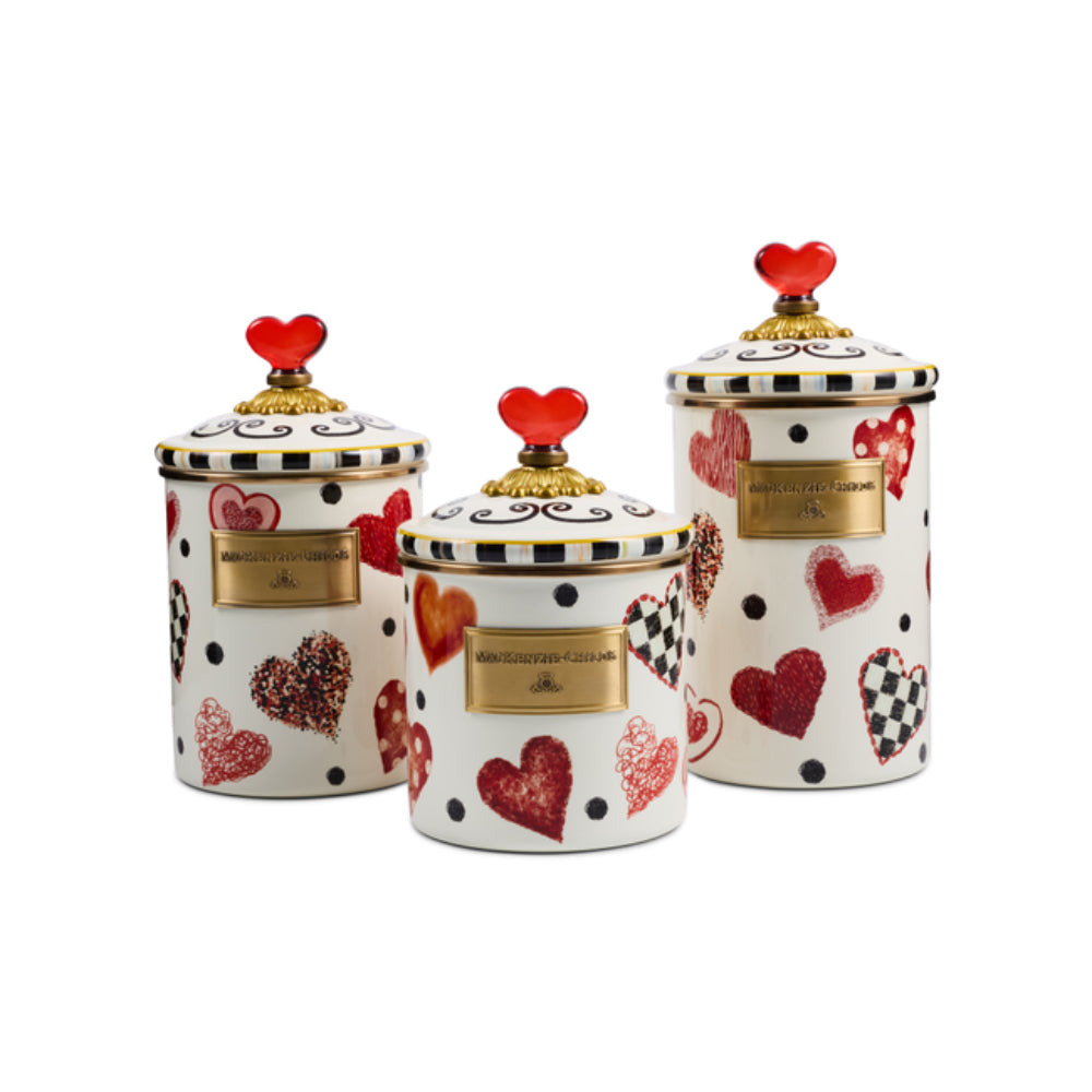 Three white ceramic canisters with red and black heart patterns, gold plaques, and red heart-shaped lids, arranged on a white background.