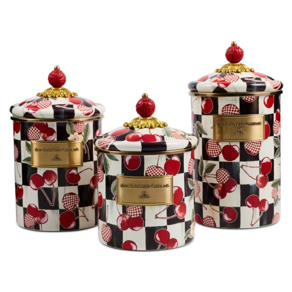Three ceramic canisters with matching lids, featuring a black and white checkerboard pattern decorated with red cherries and gold-tone metal plaques on the front.