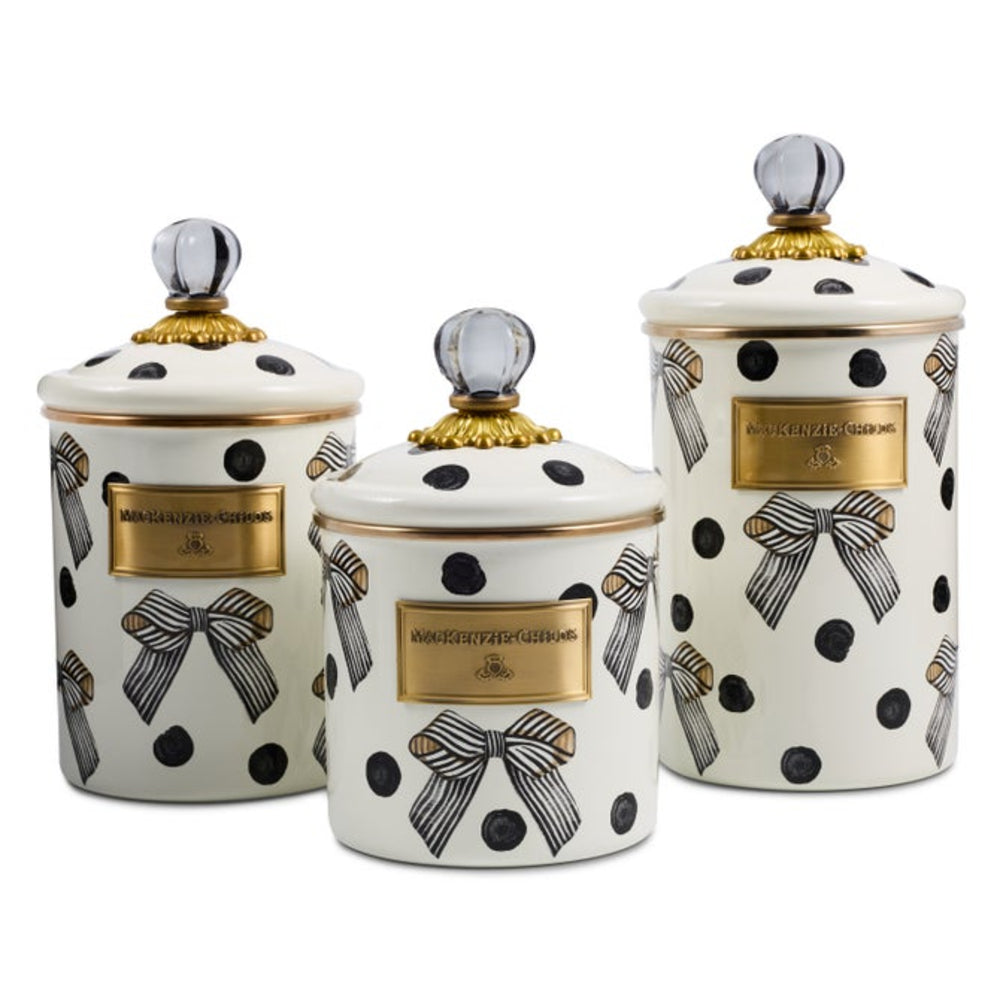 Three ceramic canisters with matching lids, decorated with black polka dots, striped bows, and gold plaques, arranged on a white background.