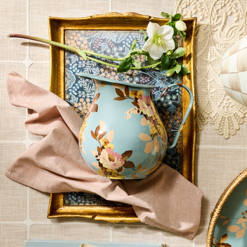 Decorative floral pitcher with a gold frame and pink cloth on a textured surface