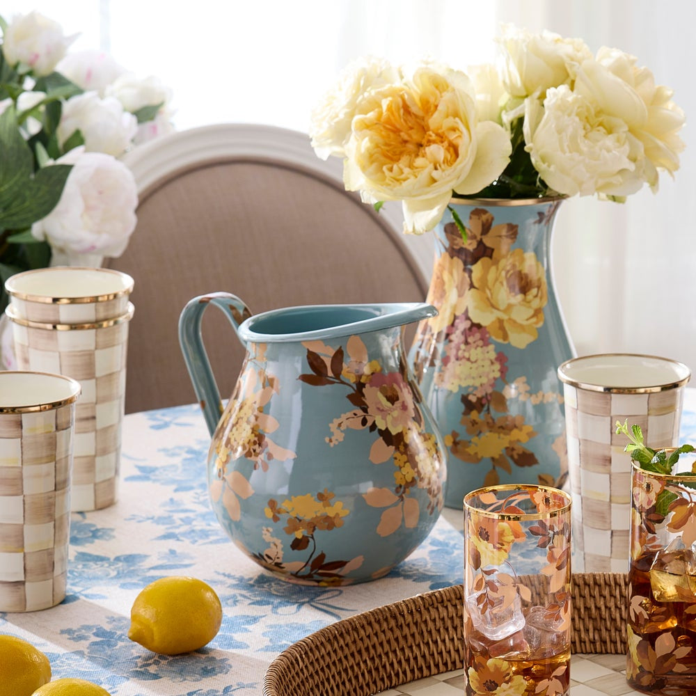 Decorative floral pitcher on a table with flowers and a glass.