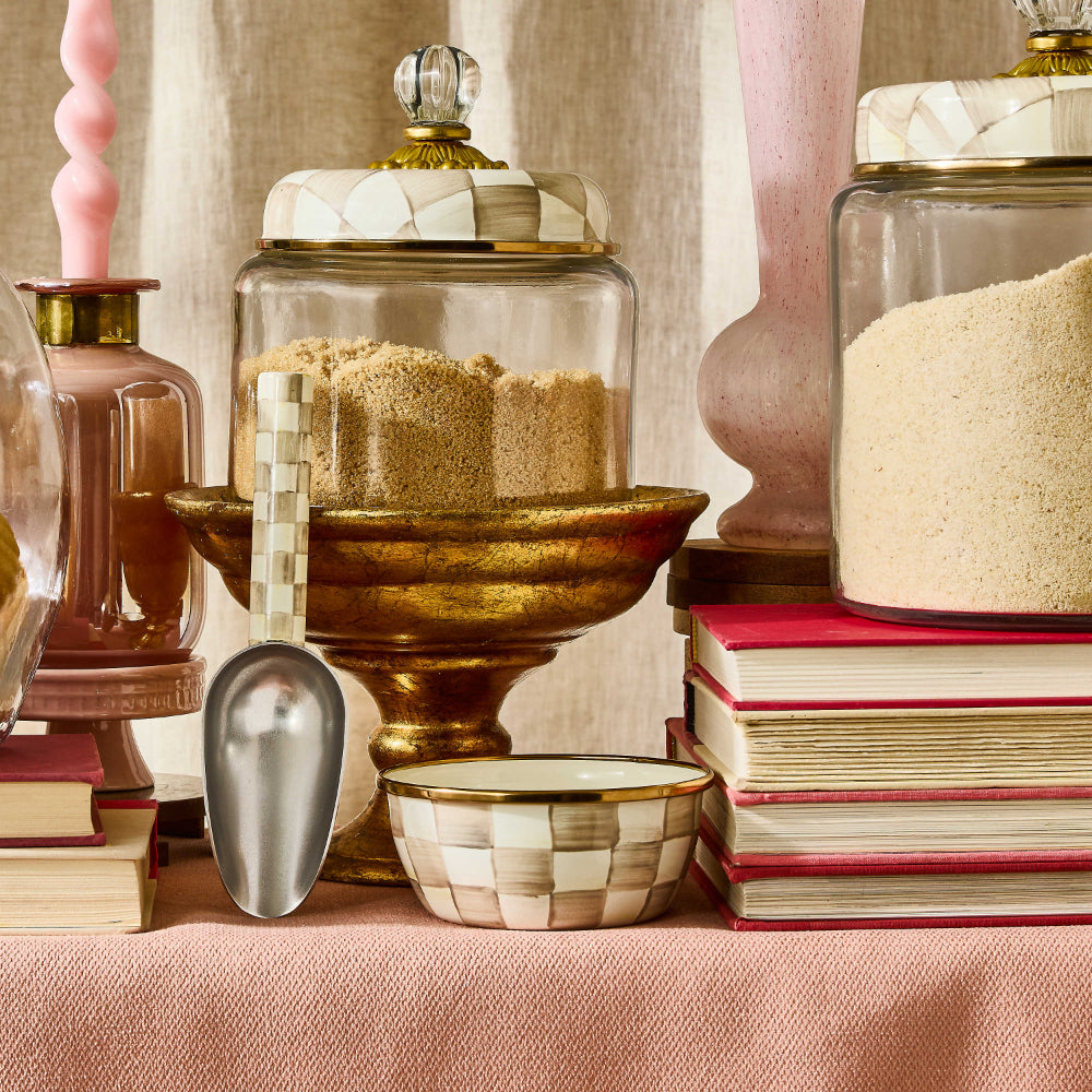 Mocha Checkered patterned bowl with gold on a shelf with food containers and books with a pink table cloth. 