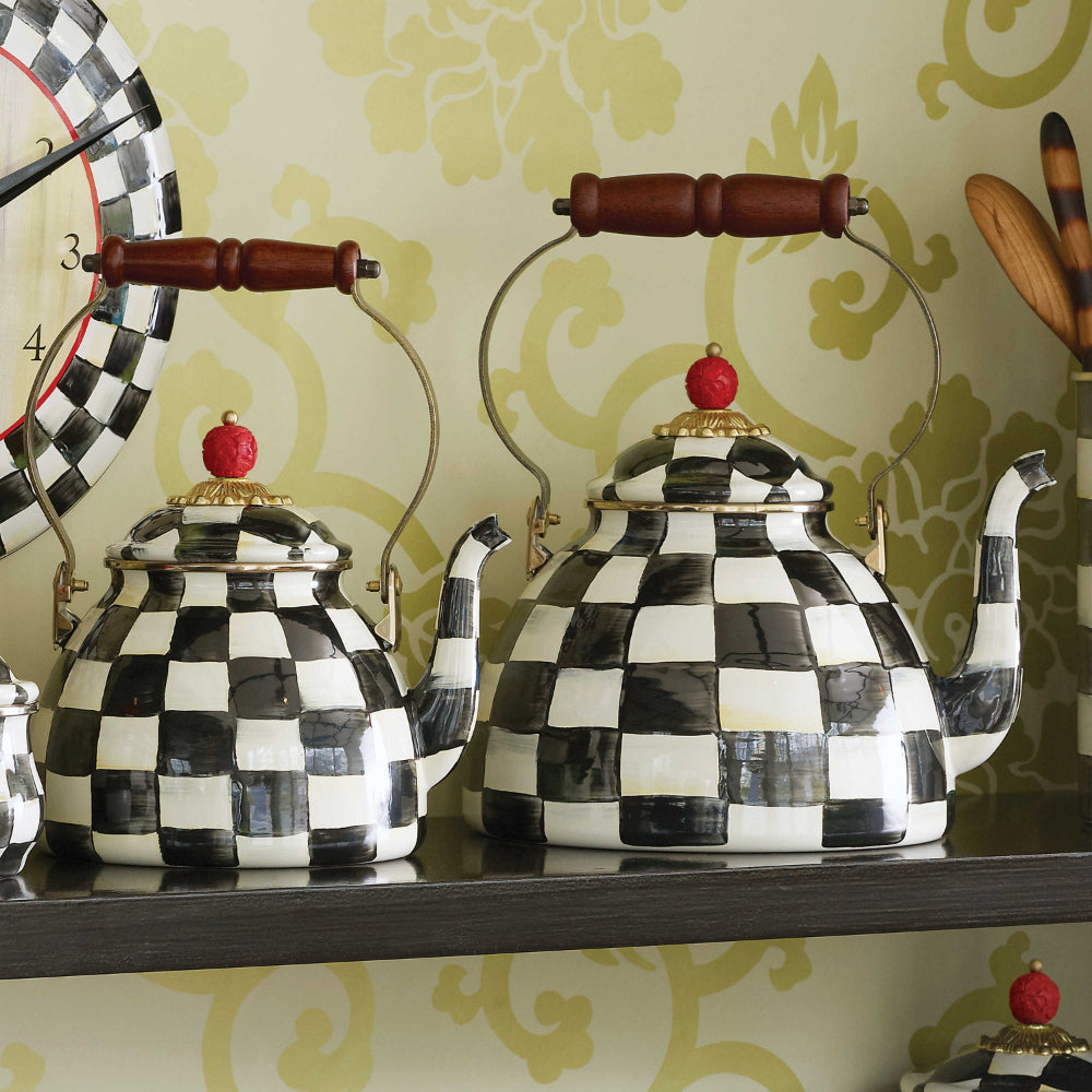  Two decorative teapots with black and white checkered pattern with handle on a shelf with a green wall in the backround.