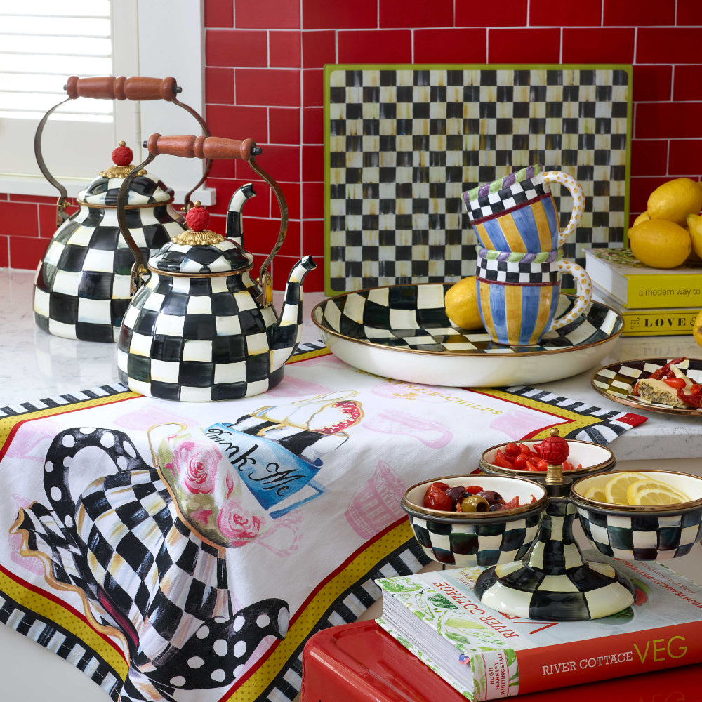 Two decorative teapots with black and white checkered pattern with handle on a table with other simular checkard items. 