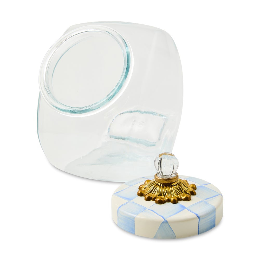 A clear glass cosmetic jar with a matching round lid featuring a blue and white checkered pattern and a gold-tone decorative finial on top, shown on a white background.