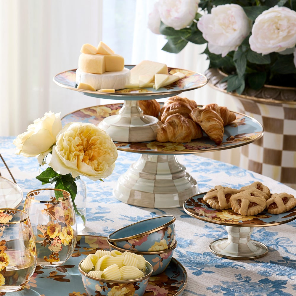 Three-tiered dessert stand with pastries on a decorative tablecloth.