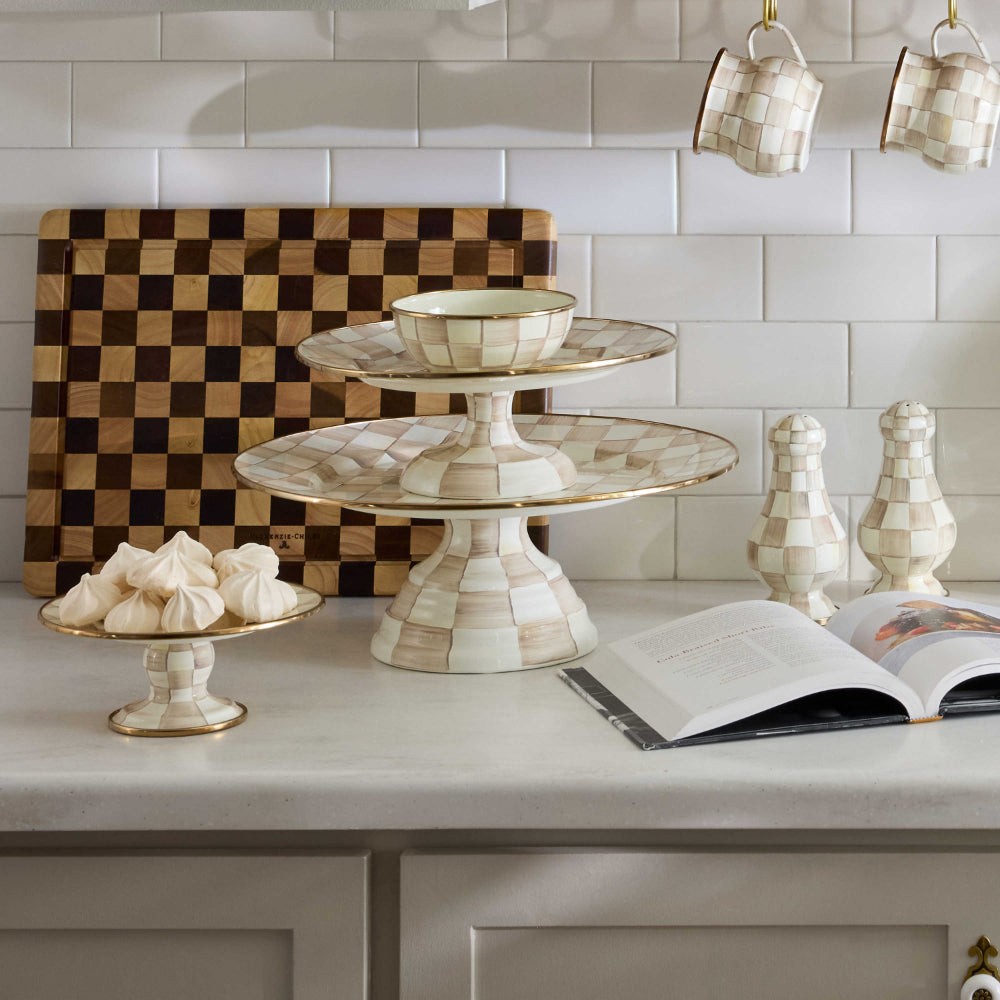 Decorative cake stand with a mocha check pattern on a white counter top with other mocha check Mackenzie enamel ware. 