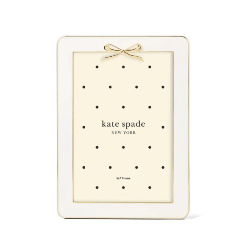 White enamel 5x7 Kate Spade New York picture frame with a gold bow on the top and polka dot pattern on a white background.