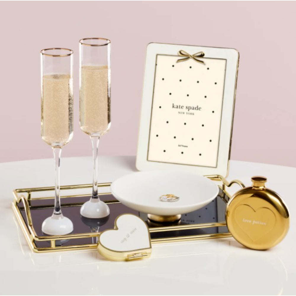Decorative items including champagne flutes, a mirror, and a heart-shaped container on a tray with a pink background.