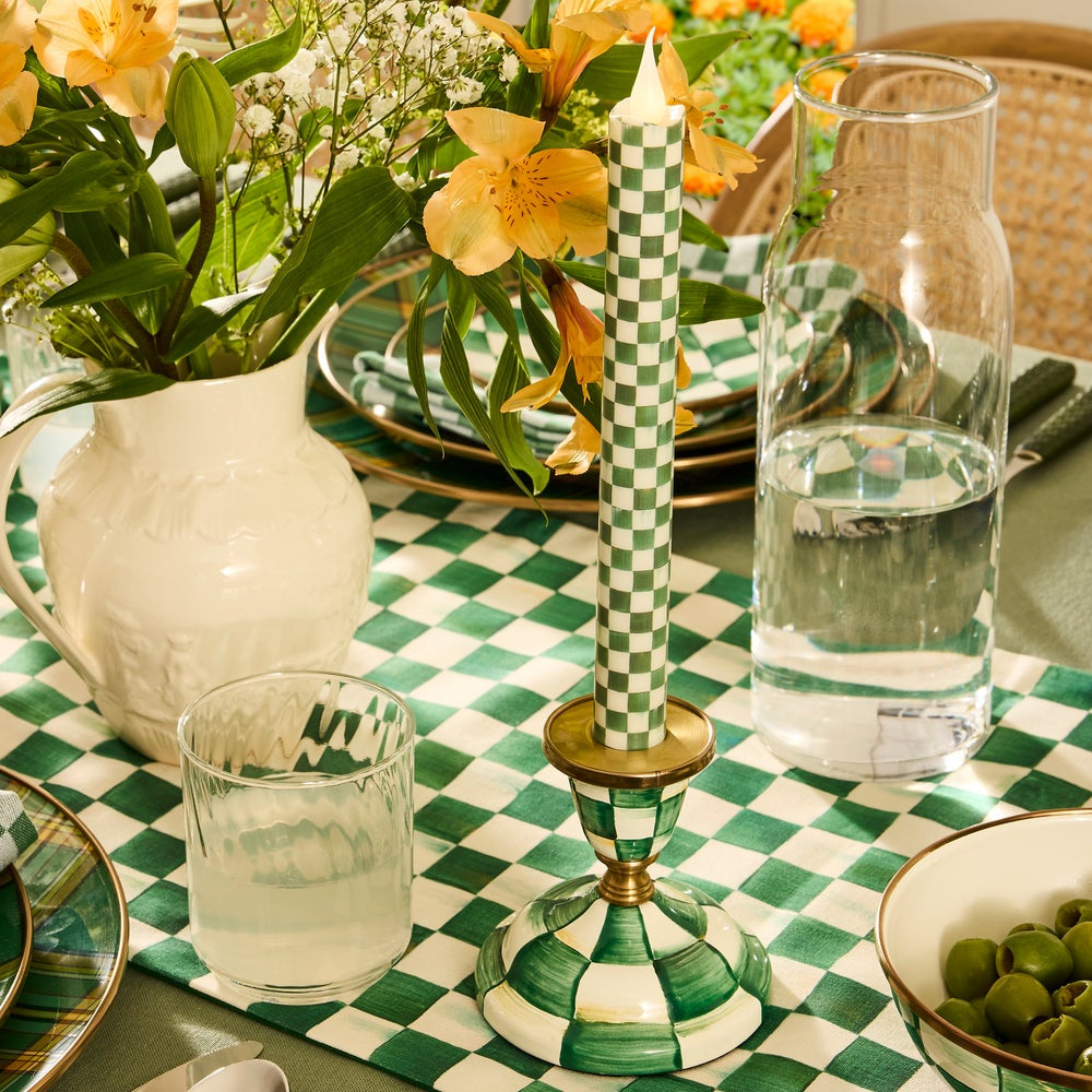 Decorative table setting with checkered tablecloth, candle, and floral arrangement.