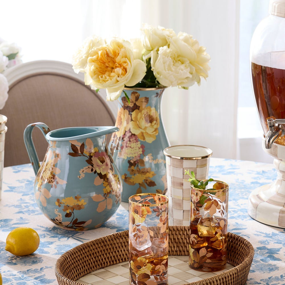 Floral-patterned pitcher and glasses on a table with a floral arrangement.