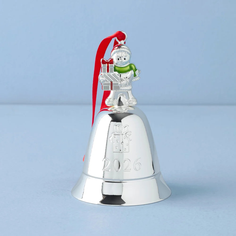 A small figurine of a gingerbread man standing on a silver bell engraved with "2026" shown on a light blue background.