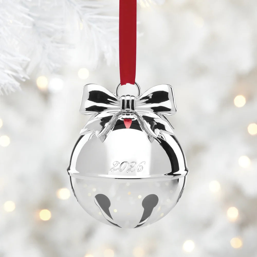 Silver bell ornament with a red ribbon on a blurred Christmas tree background