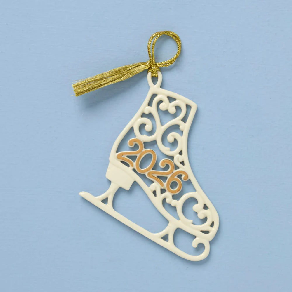 A decorative ice skate-shaped ornament in cream-colored wood with intricate cutout scrollwork and a gold-colored hanging loop and tassel. The year '2026' is cut out in the center in a warm gold tone.