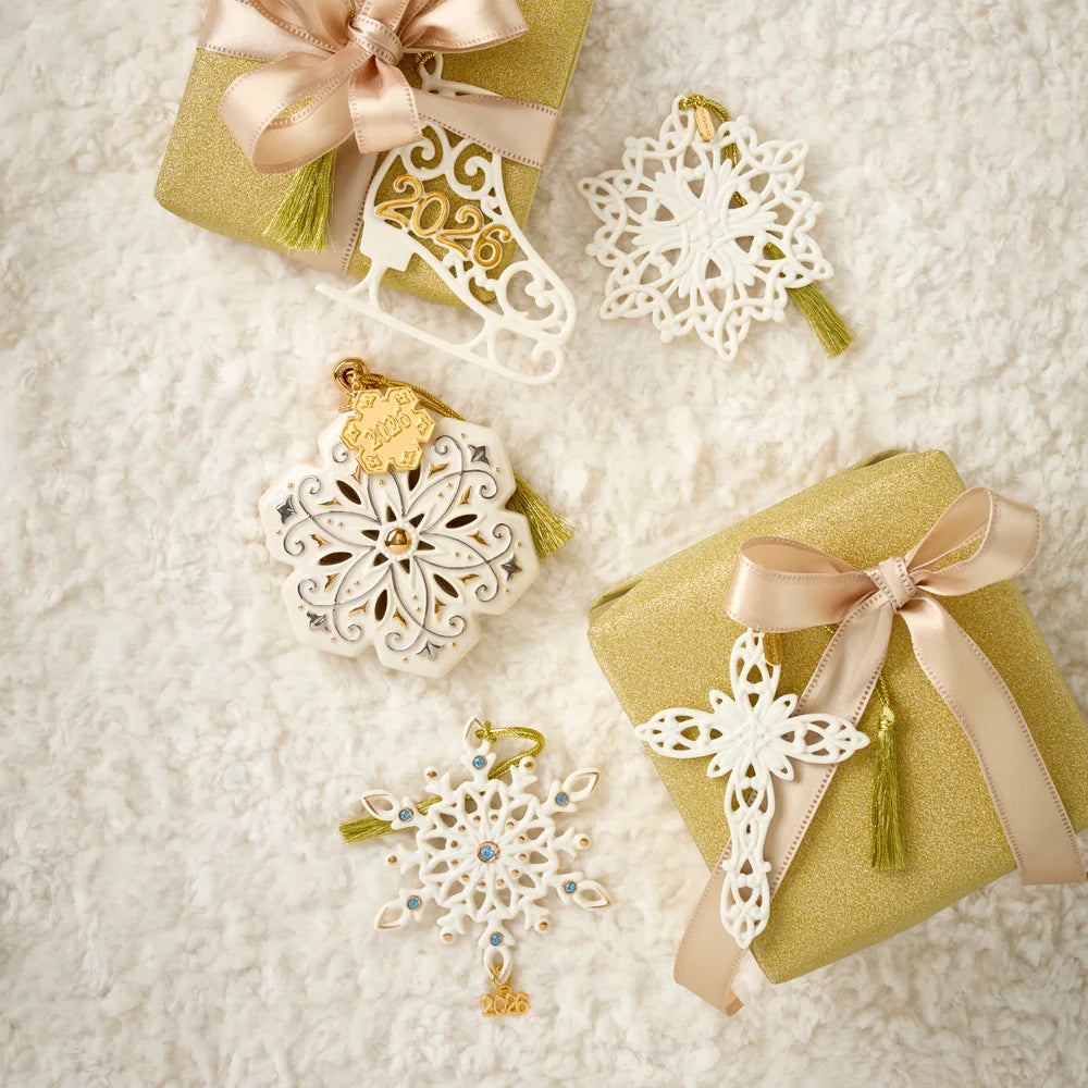 A collection of Christmas ornaments arranged on a beige fabric background with red ribbon garlands. The ornaments include a boot-shaped ornament, a cross ornament, and two snowflake ornaments