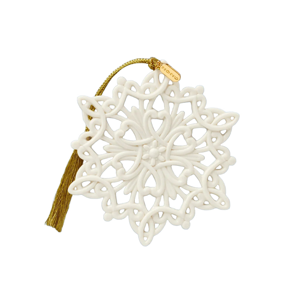 An off-white ceramic snowflake Christmas ornament with intricate cutouts, a gold tassel, and a gold hanging string on a plain white background.