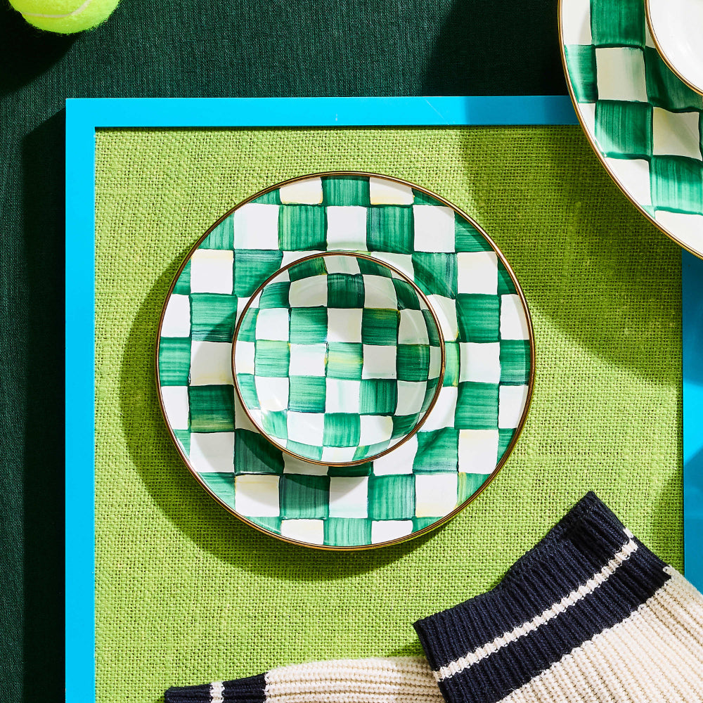 Checkered ceramic bowl with green and white pattern on a on a green place matted table with other simular items. 
