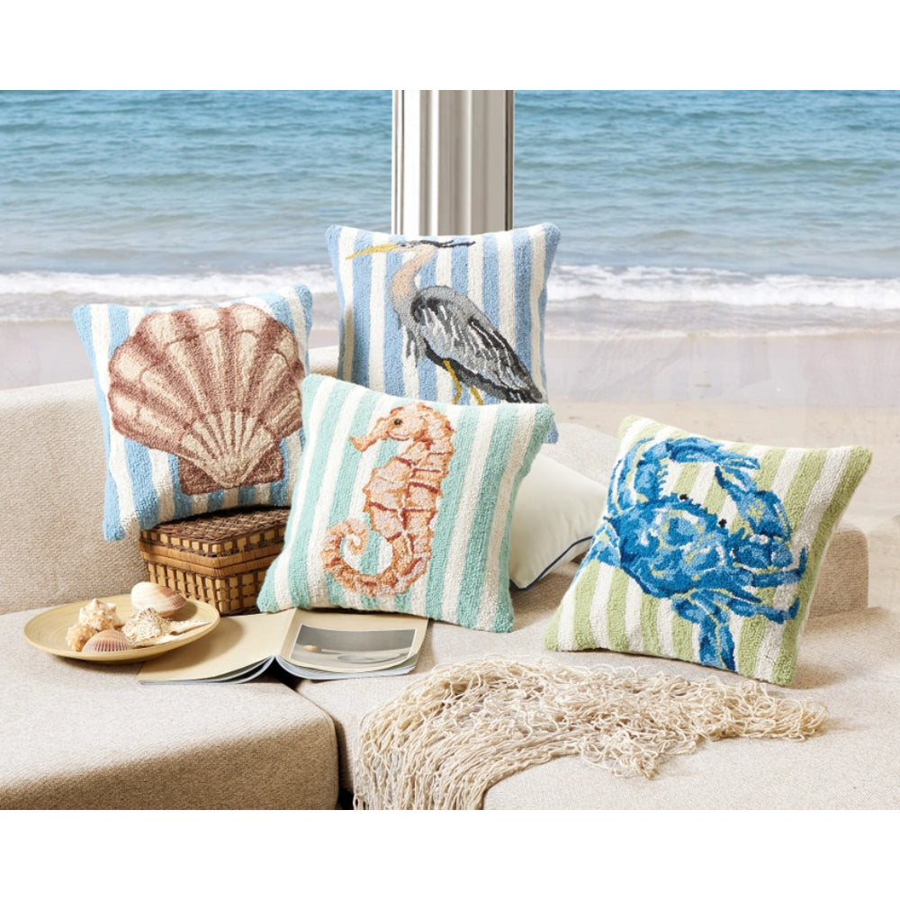 Decorative pillows with seashell, bird, and floral patterns on a couch by a window with a beach view.